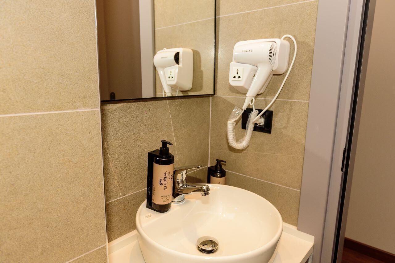 A bathroom with a sink, a mirror, a hairdryer, and a bottle of shampoo.