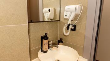 A bathroom with a sink, a mirror, a hairdryer, and a bottle of shampoo.