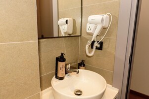 A bathroom with a sink, a mirror, a hairdryer, and a bottle of shampoo.