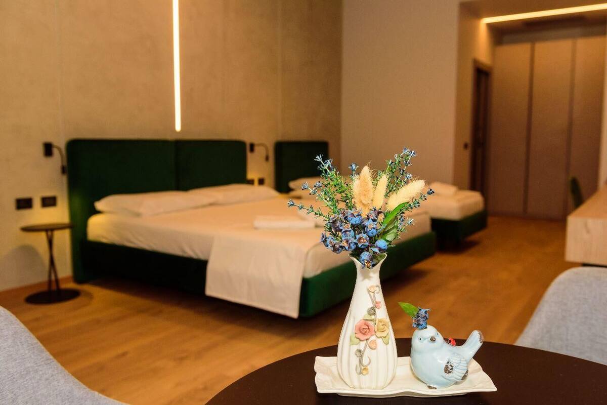 A hotel room with a green bed, a vase with flowers, and a bird figurine on a table.