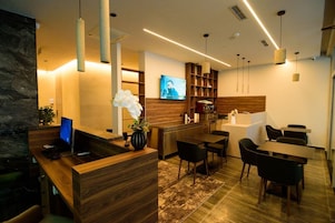 Un área de recepción moderna con un mostrador de madera, una computadora, un televisor y una zona de estar con sillas y una mesa.