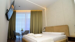 A hotel room with a bed, a desk with a chair, a TV mounted on the wall, and a window with curtains. - Hotel Zeneli Vlore (Vlorë)