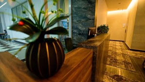 A reception desk with a vase of flowers, a marble wall, and a checkered floor. - Hotel Zeneli Vlore (Vlorë)