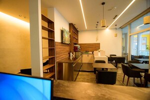 Una cocina moderna con electrodomésticos de acero inoxidable, estantes de madera y una zona de estar con mesas y sillas.