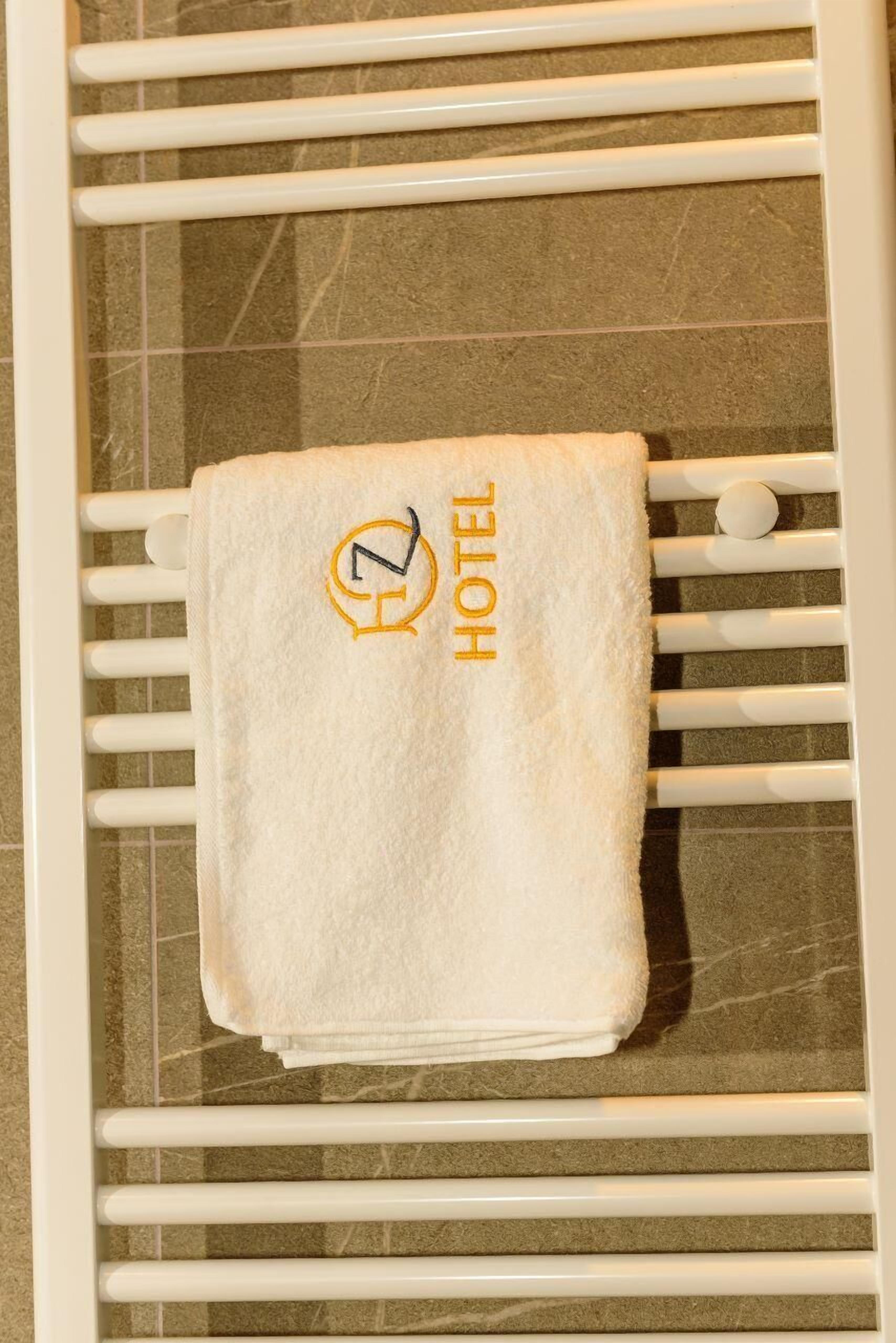 Une serviette blanche ornée du logo d’un hôtel et du mot « HÔTEL », posée sur un porte-serviettes blanc.
