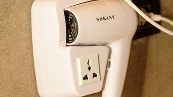 A white hairdryer plugged into a wall socket with a cord.