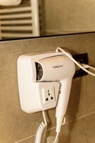 A white hairdryer plugged into a wall socket with a cord.