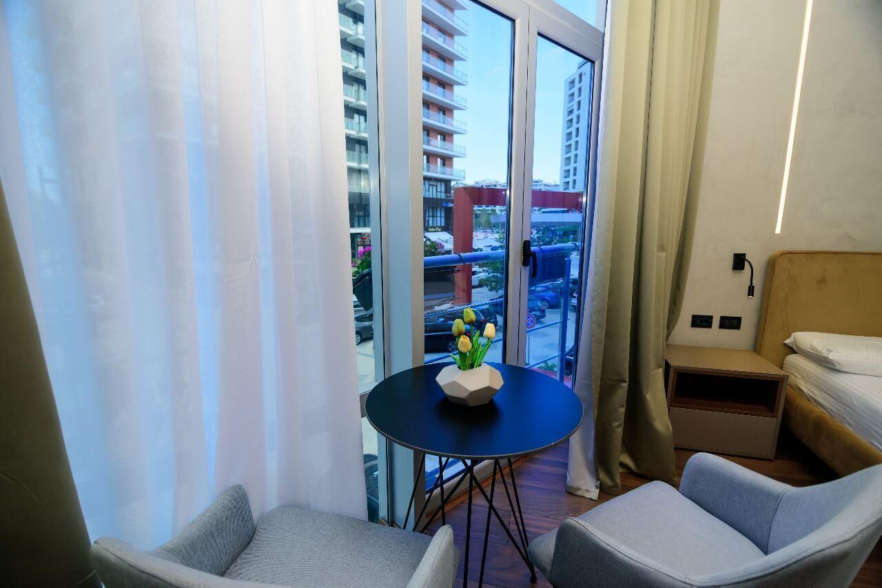 A hotel room with a balcony, a small table with a vase of flowers, a bed, and a chair.