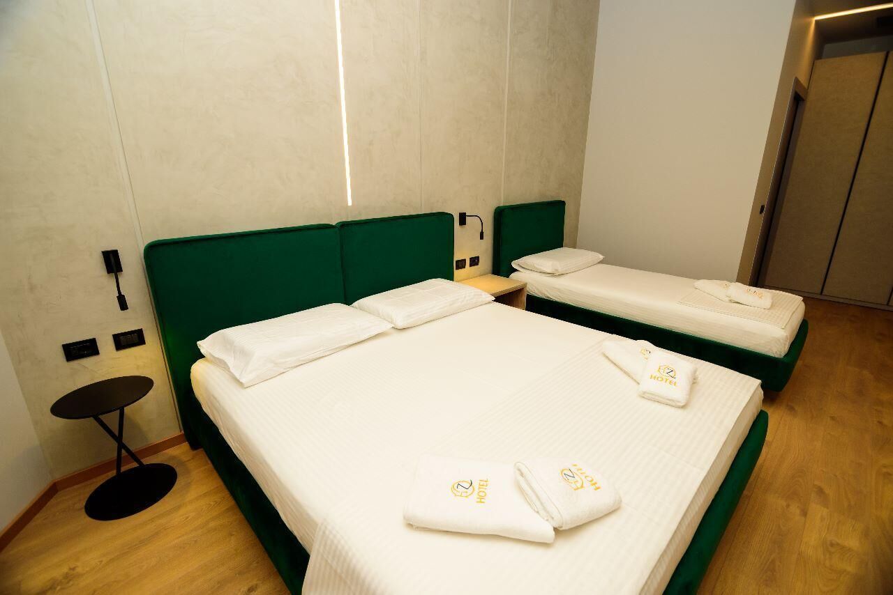 Una habitación de hotel con dos camas, una mesita y un enchufe para cargar dispositivos en la pared.