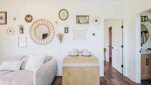A modern living room with a sofa, a wooden side table with dishes, and various wall decorations including framed pictures and a mirror. - Walk2OldTown!  Modern Lux Private Carriage House (Bluffton)
