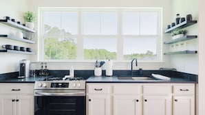 A modern kitchen with white cabinets, a black countertop, a stove, and a window with a view of trees. - Walk2OldTown!  Modern Lux Private Carriage House (Bluffton)