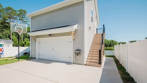 A residential garage with a basketball hoop, a white garage door, and a wooden staircase leading to a deck. - Walk2OldTown!  Modern Lux Private Carriage House (Bluffton)
