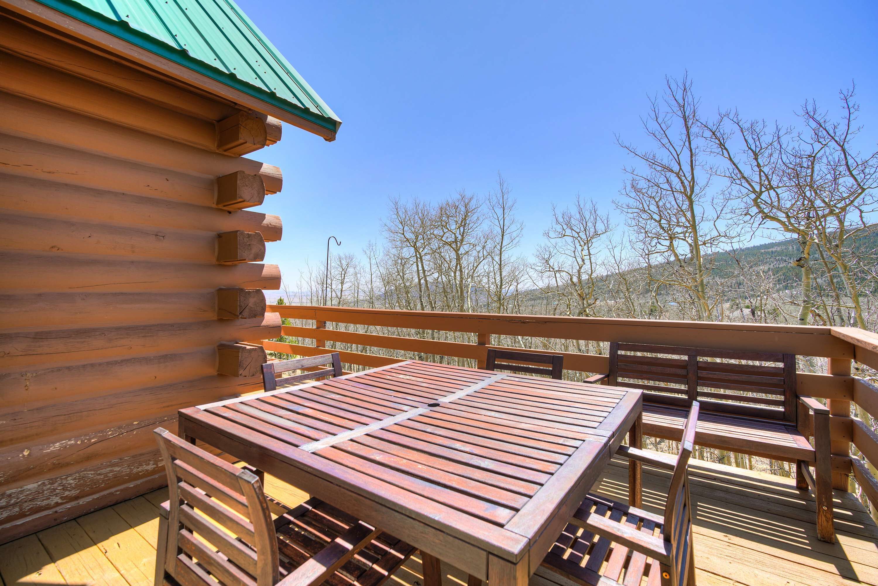 A wooden deck with a table and chairs, overlooking a mountainous landscape.