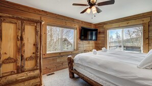 Une chambre située dans un chalet en rondins, avec un lit, un ventilateur de plafond, une télévision et de grandes fenêtres.