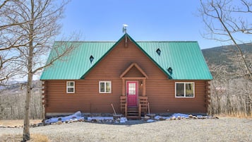 Rustic cabin with a central entrance, flanked by two windows, set amidst a tranquil natural landscape.