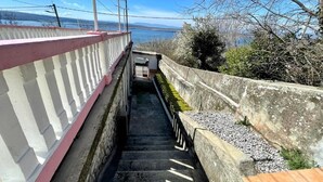 En trappa av betong med ett vitt och rosa räcke, som leder upp till en högre nivå med utsikt över havet och bergen i bakgrunden.