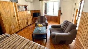 Ett mysigt vardagsrum med en soffa, en fåtölj och ett soffbord. Det finns ett träskåp och en tv-apparat på ett TV-bord.