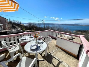 A terrace with white plastic chairs and tables, a pink railing, and a view of a lake. - Holiday house Luky (Dramalj)