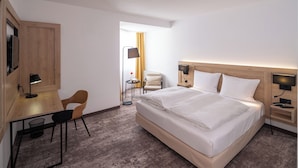 Una habitación de hotel con cama, escritorio, silla y una mesita de noche con lámpara.