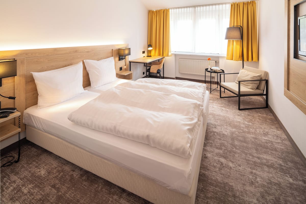 Ein Hotelzimmer mit einem großen Bett, einem Schreibtisch, einem Stuhl und einem kleinen Tisch mit einer Lampe.