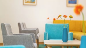 Un rincón de descanso con sillas grises y azules, una mesa de madera y un jarrón azul con flores.