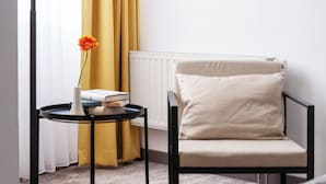 Una habitación moderna con una lámpara de pie, una mesita con un florero y libros, una silla y un radiador.