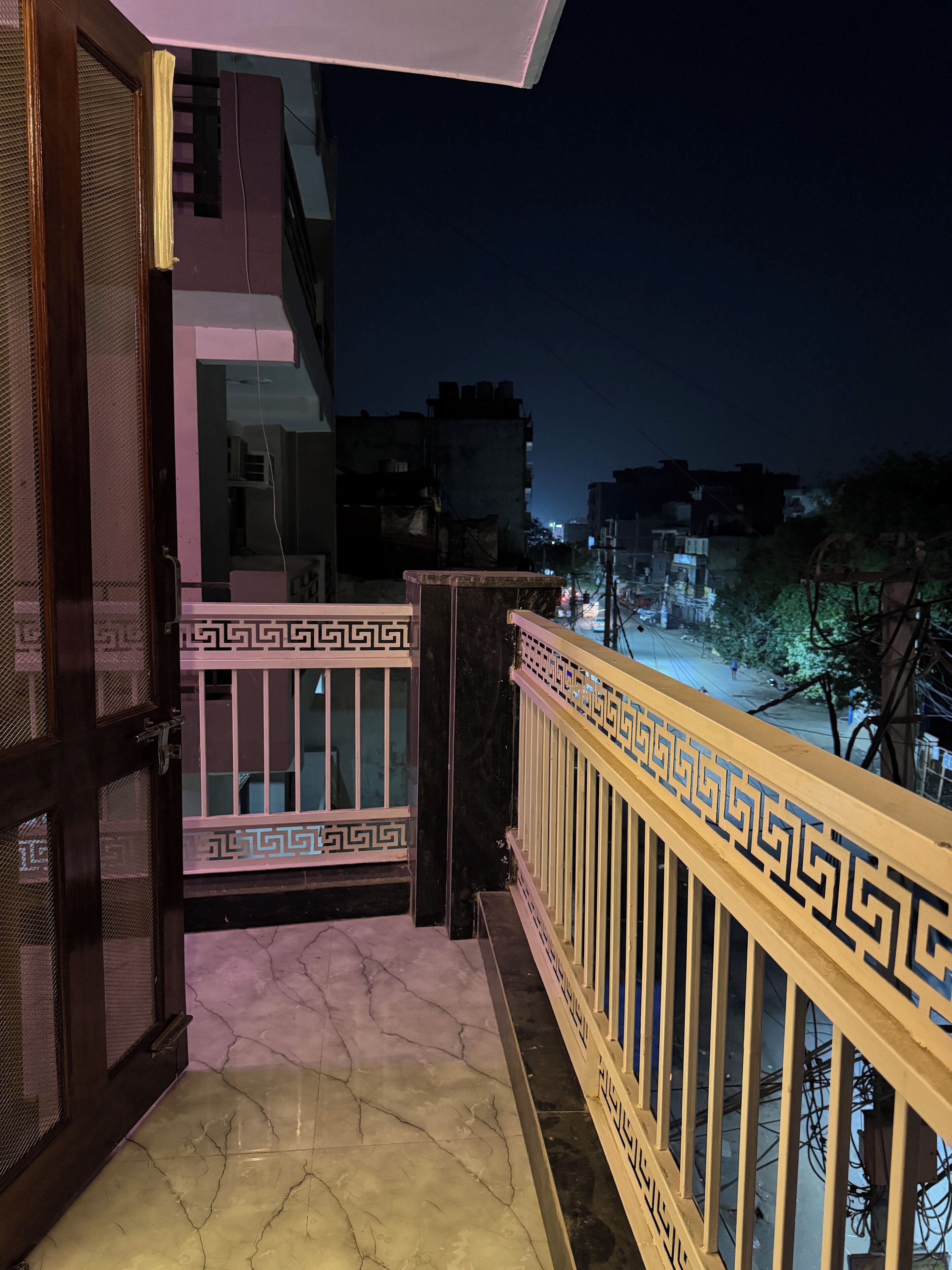 A balcony with a patterned railing, a door with a mesh screen, and a view of the cityscape at night.