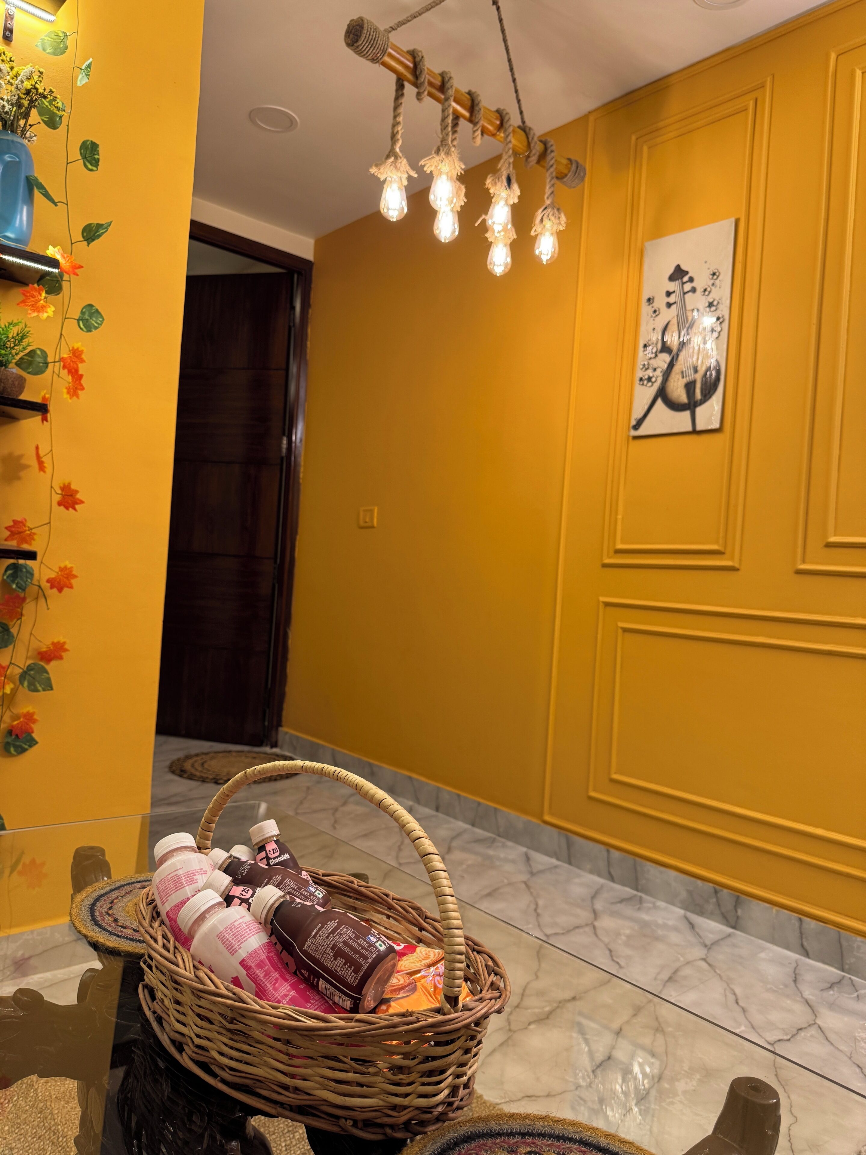 A room with a yellow wall, a wooden door, a wicker basket with bottles, and a light fixture.