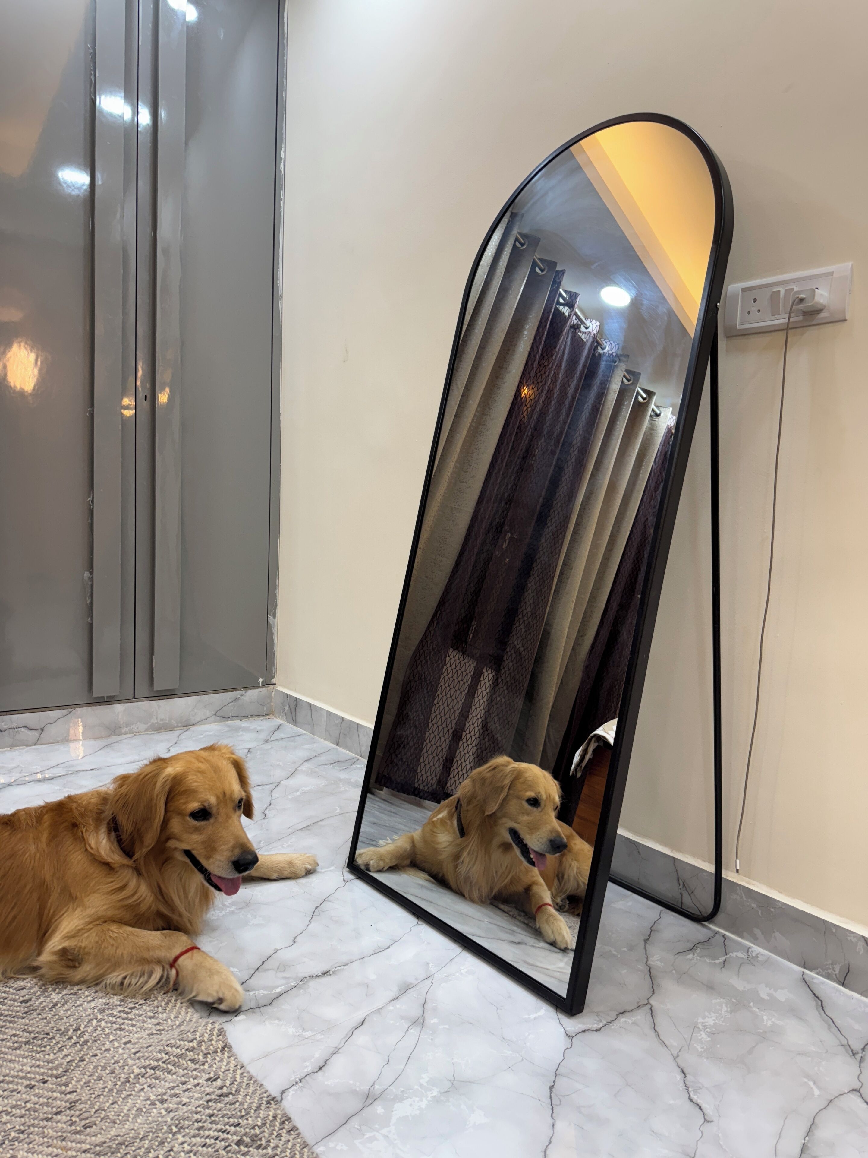 A dog lying on a marble floor next to a mirror reflecting a curtain.