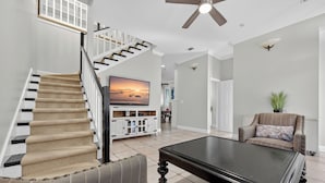 A spacious living room with a staircase, a flat-screen TV, a coffee table, and a sofa. - Rue Caribe* Fire pit, special Fall Rates, community pool * Salt Water Vacations (Miramar Beach)