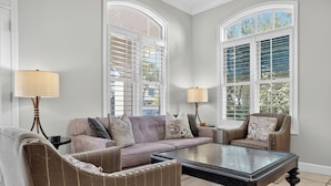 A living room with a sofa, two armchairs, a coffee table, and two lamps. There are large windows with shutters. - Rue Caribe* Fire pit, special Fall Rates, community pool * Salt Water Vacations (Miramar Beach)