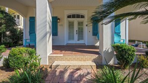 A building with a white facade, teal shutters, and a covered entrance with steps leading to a door. - Rue Caribe* Fire pit, special Fall Rates, community pool * Salt Water Vacations (Miramar Beach)