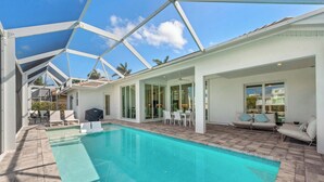 Ein moderner Poolbereich mit einem klaren, blauen Pool, weißer Gartenmöbel und einer überdachten Terrasse.
