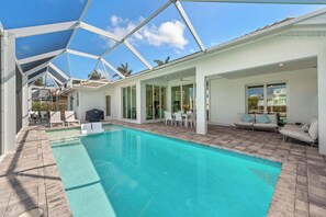 Ein moderner Poolbereich mit einem klaren, blauen Pool, weißer Gartenmöbel und einer überdachten Terrasse.
