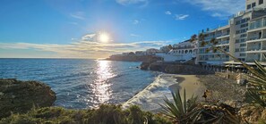 Un hotel frente al mar con vista a la playa, un litoral rocoso y cielo despejado.
