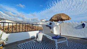 A hotel rooftop terrace with a thatched umbrella, lounge chairs, and a patterned rug.