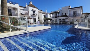 A swimming pool surrounded by white buildings with balconies, clear blue sky, and a sunny day.