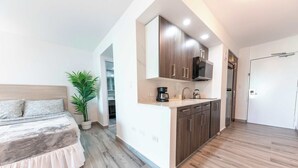 Un dormitorio moderno con una cama grande, una pequeña cocina con armarios de madera y una planta en maceta.