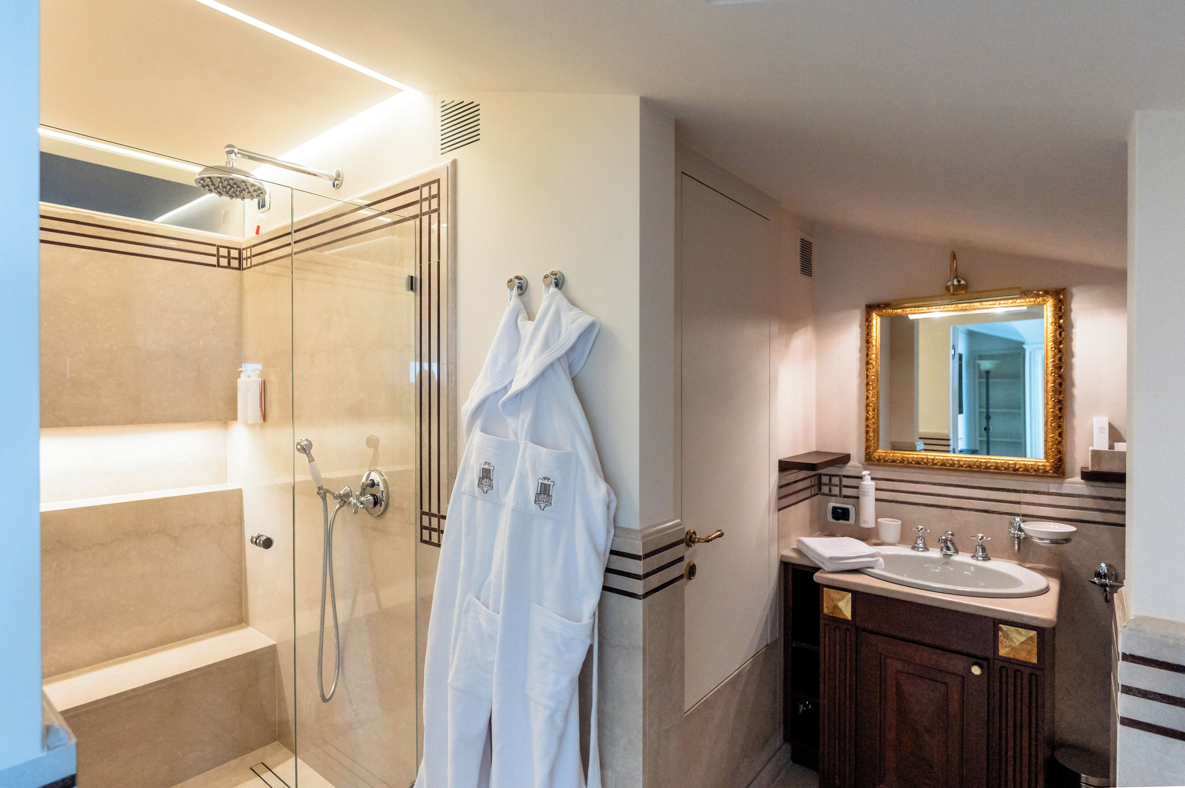 Une salle de bain moderne avec une douche à parois de verre, un meuble-lavabo avec un évier et un miroir, et un peignoir accroché au mur.