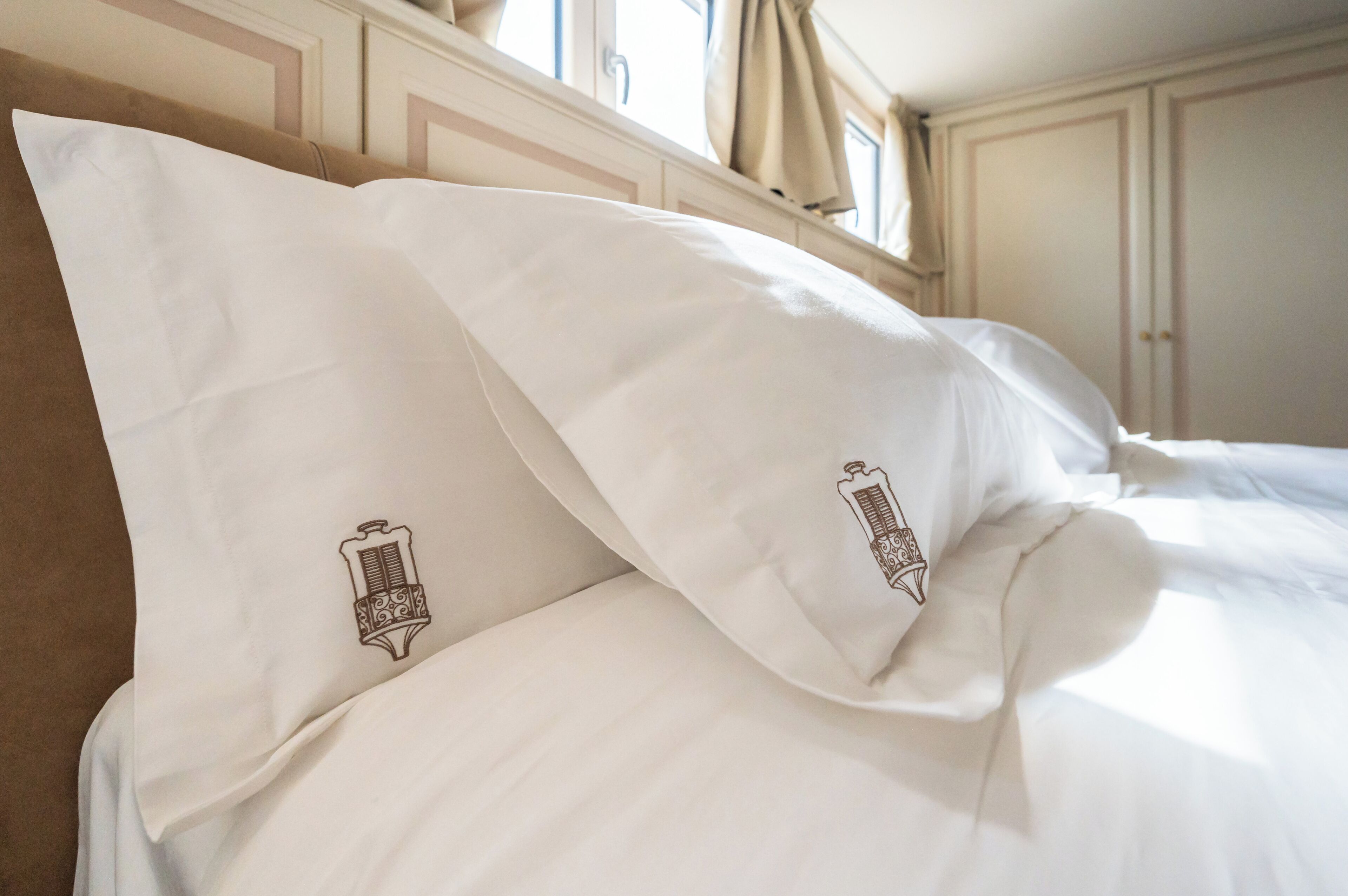 Un lit bien fait, avec du linge de lit blanc et deux oreillers ornés d’un motif représentant une harpe.