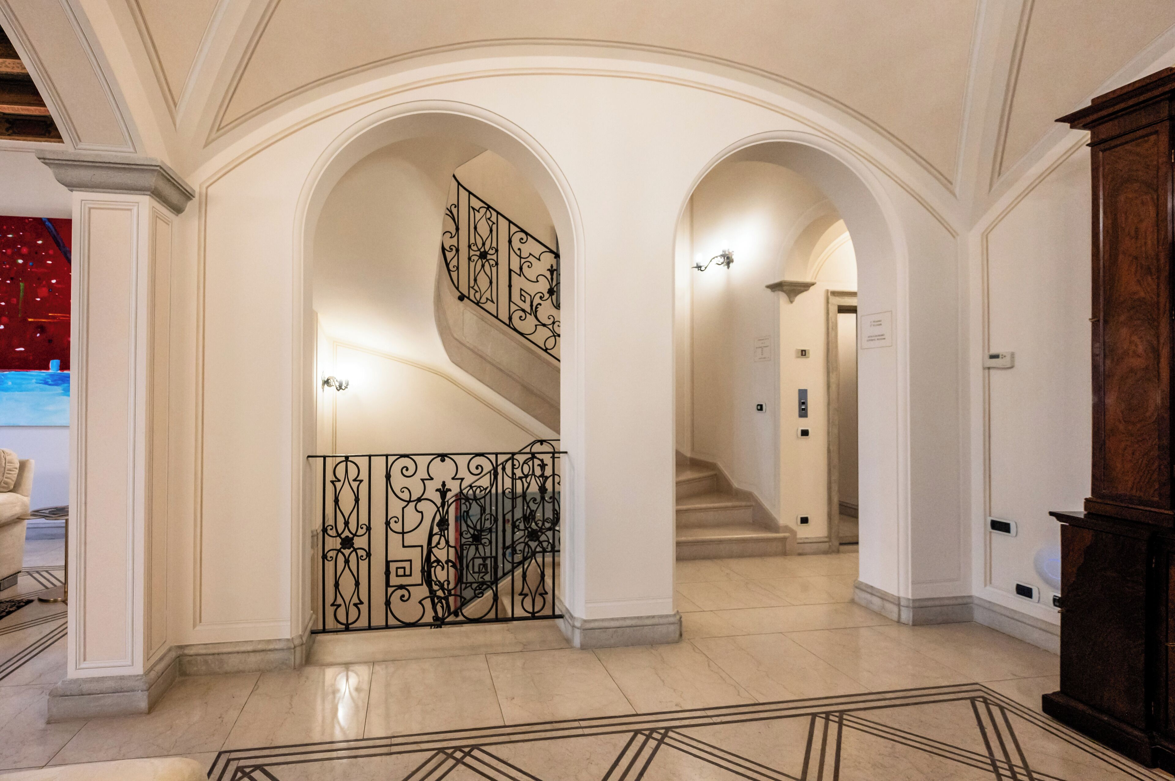 A grand hallway with a marble floor, ornate iron railings, and a staircase leading to another level.