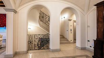 A grand hallway with a marble floor, ornate iron railings, and a staircase leading to another level.