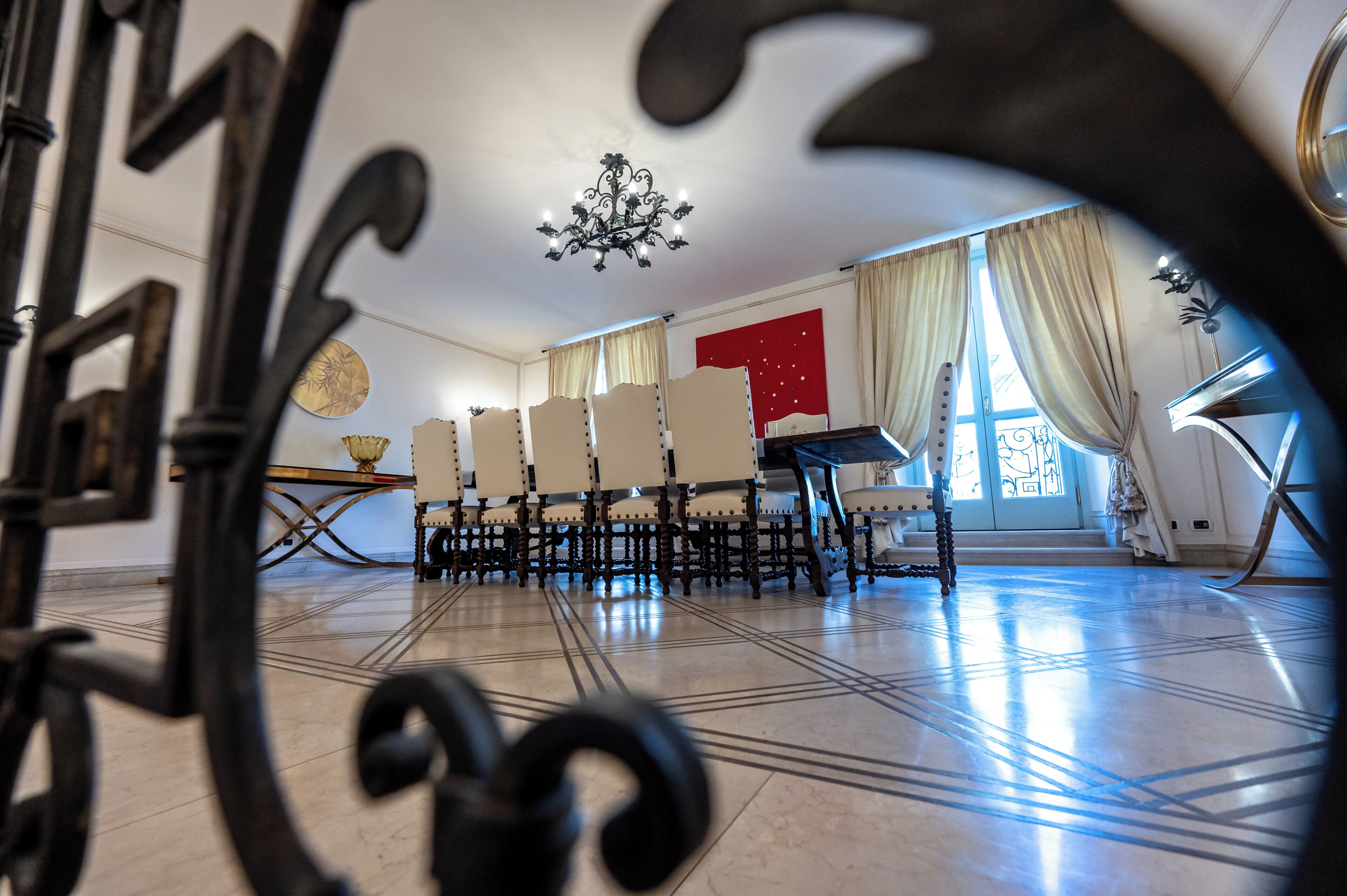Una stanza con un lampadario, un pianoforte e un'ampia finestra con tende.