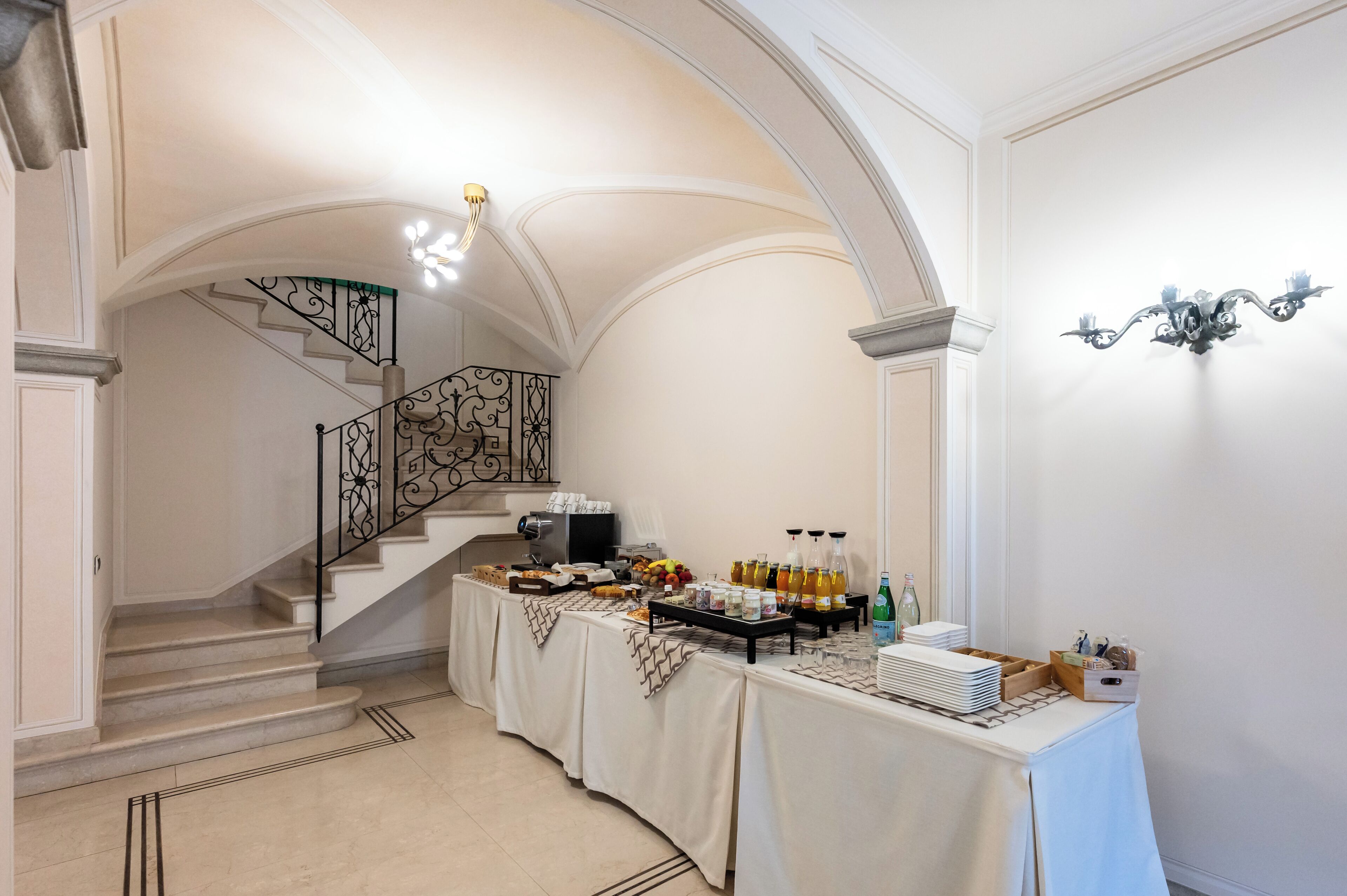 A spacious room with a staircase, a buffet table with food and drinks, and elegant wall sconces.