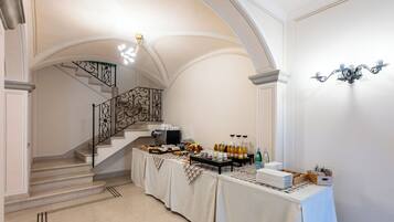 A spacious room with a staircase, a buffet table with food and drinks, and elegant wall sconces.