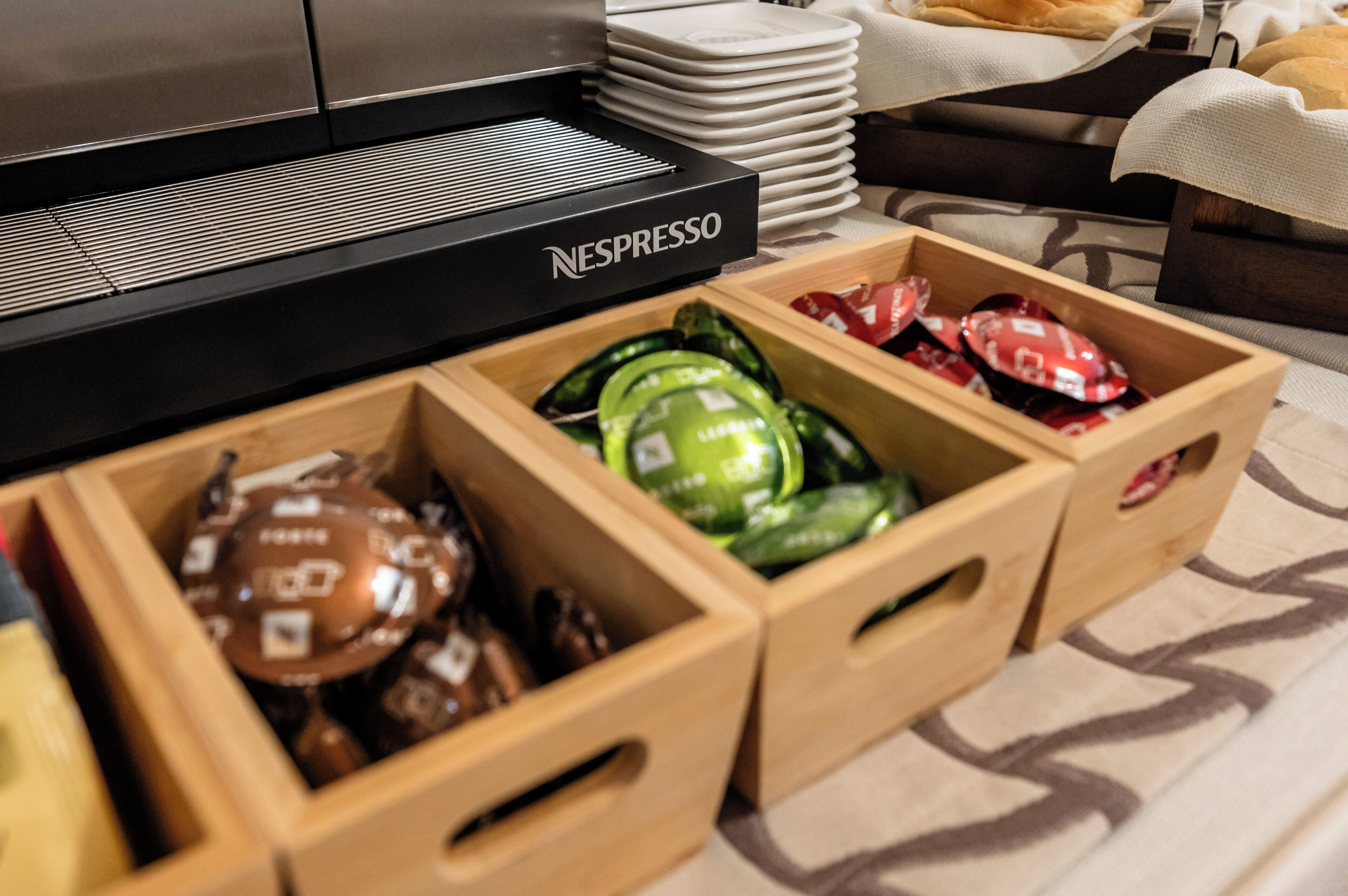 A coffee station with a Nespresso machine and various coffee pods in wooden boxes.