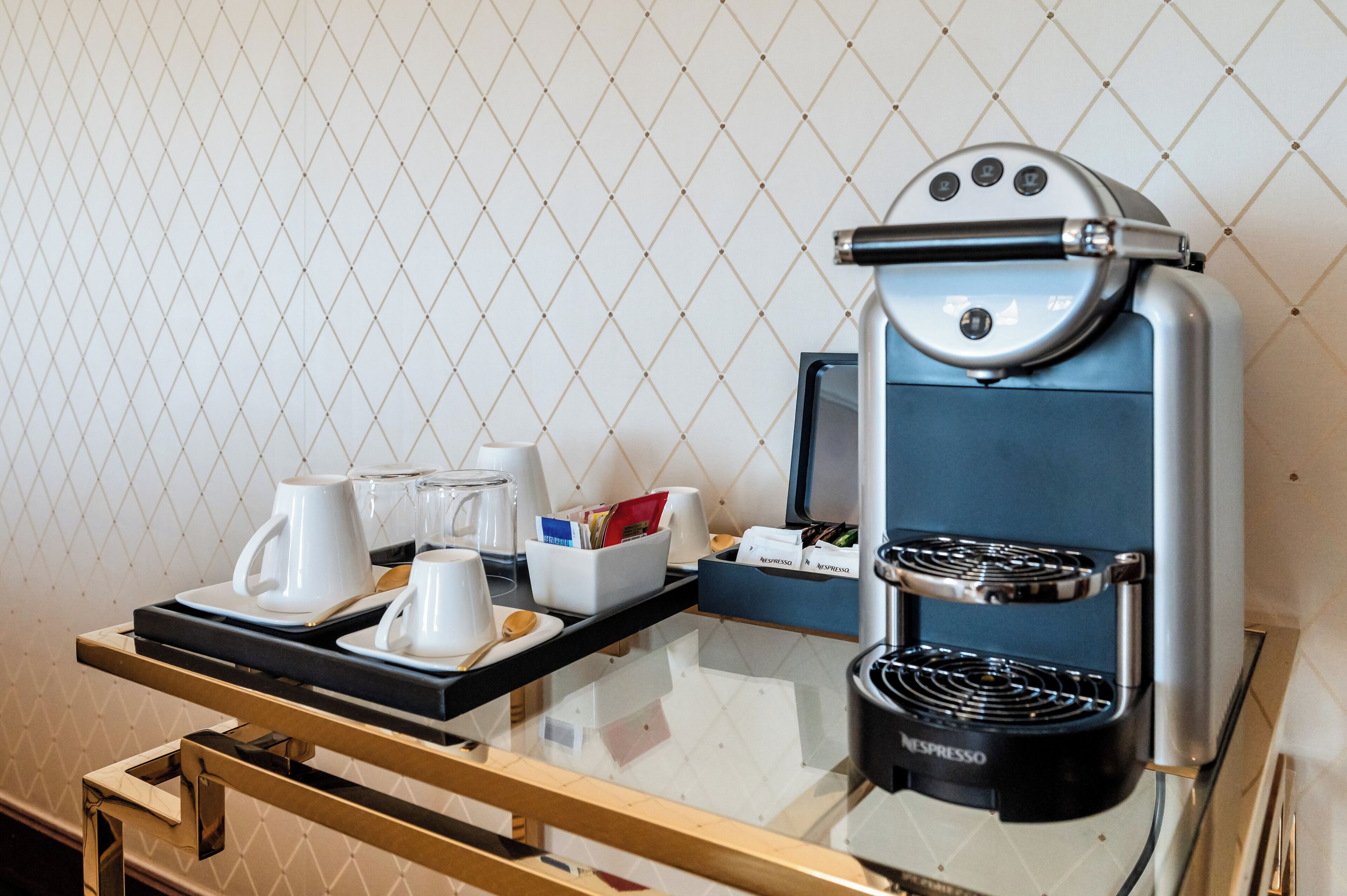A Nespresso coffee machine on a tray with cups and a sugar bowl, set against a tiled wall.