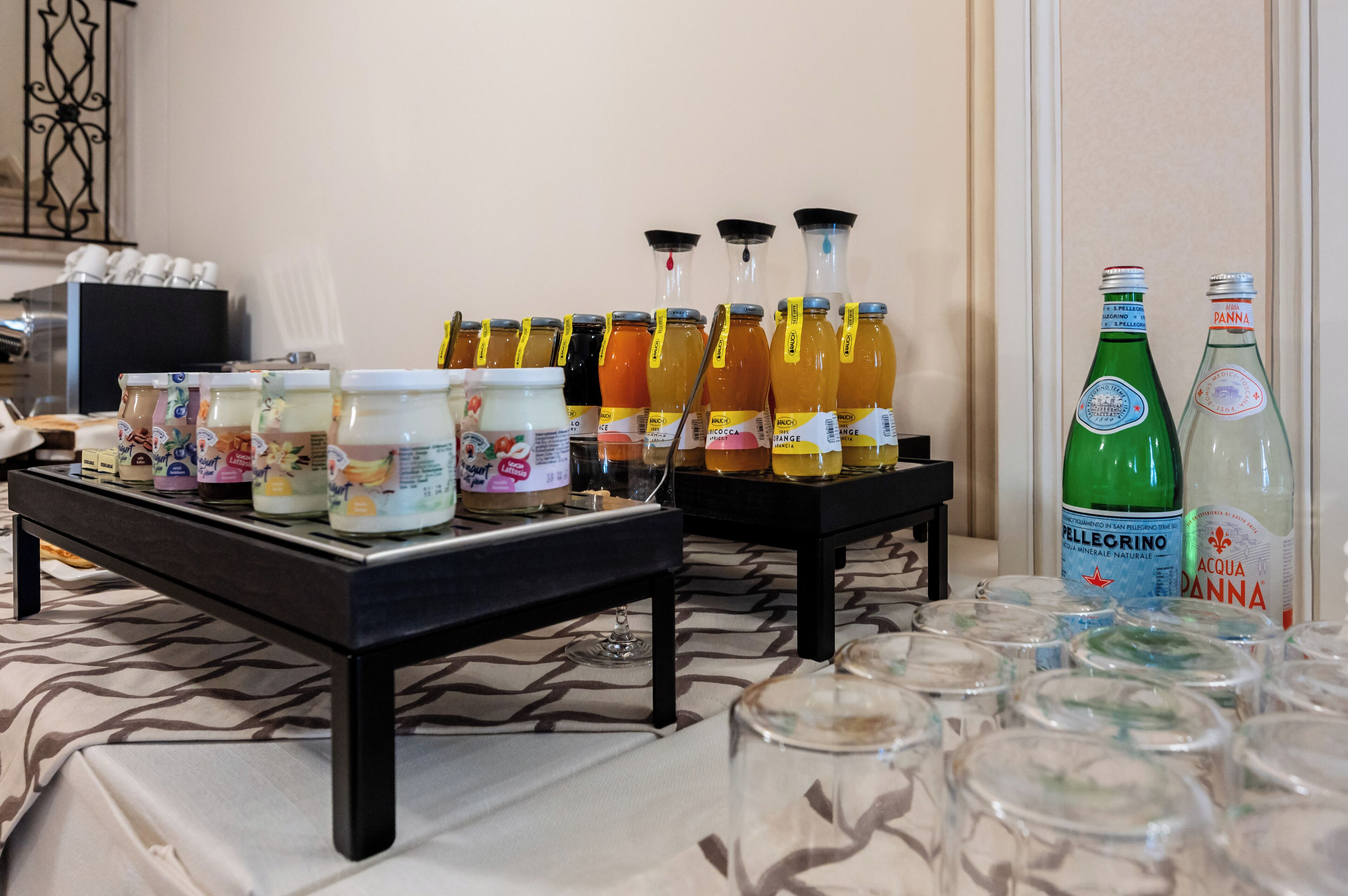 Una mesa de bufé con diversos alimentos y bebidas, incluyendo frascos de salsas, botellas de jugo y botellas de agua.