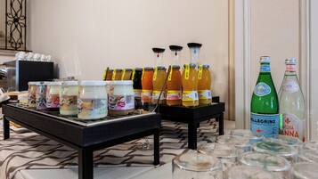 Una mesa de bufé con diversos alimentos y bebidas, incluyendo frascos de salsas, botellas de jugo y botellas de agua.