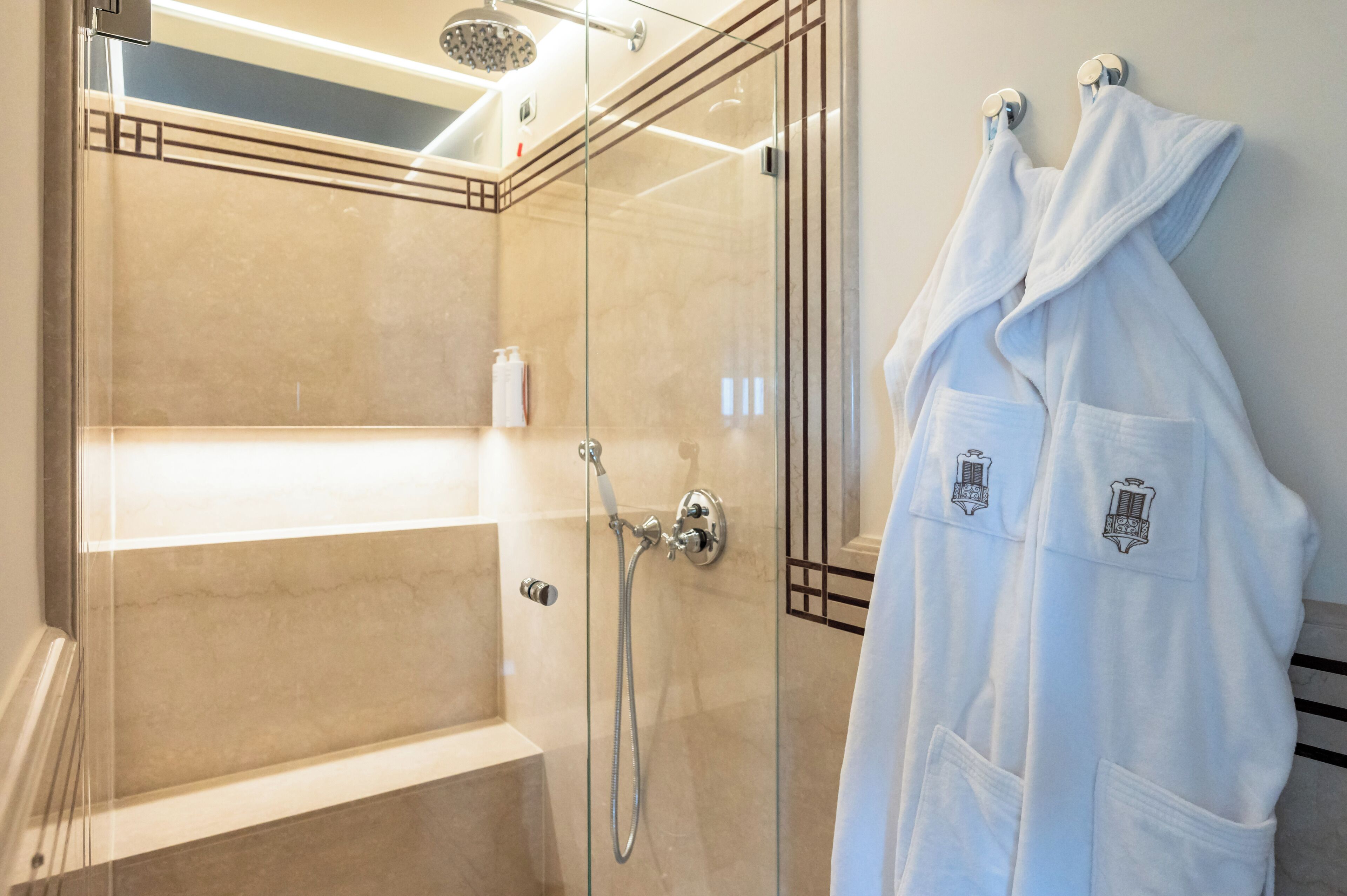 Ein modernes Badezimmer mit einer einachigen Duschkabine, einer Badewanne und zwei weißen Bademänteln, die an einer Wand hängen.